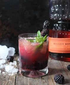 a glass filled with ice and blackberries on top of a wooden table