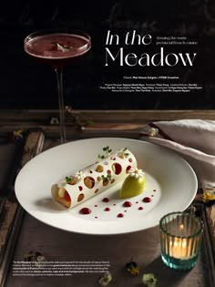 a white plate topped with food next to a glass filled with liquid and a candle