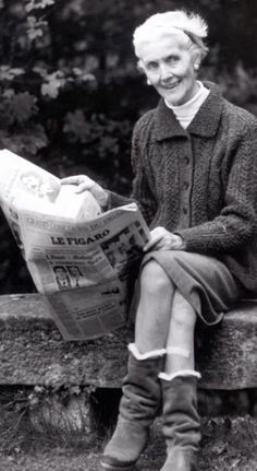 an old photo of a woman sitting on a bench reading a newspaper and smiling at the camera