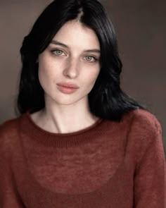 a woman with long black hair wearing a brown sweater