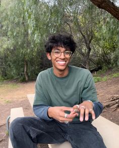 a young man sitting on top of a bench next to a forest filled with trees