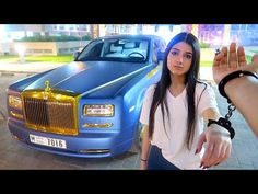 a woman taking a selfie next to a blue rolls royce parked in front of a building