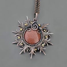 a silver and red necklace with an orange stone in the center on a gray background