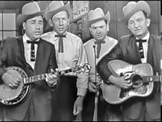 three men in suits and hats are holding guitars while one man is singing into a microphone