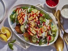 a white plate topped with a salad covered in dressing next to two silver spoons