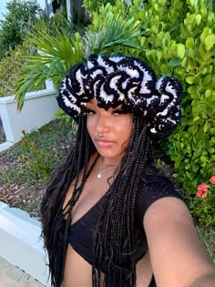 a woman wearing a black and white crochet hat in front of some bushes