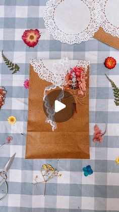 paper flowers and doily laid out on a checkered tablecloth, with scissors