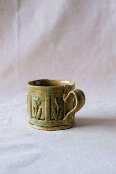 a green ceramic cup sitting on top of a white table