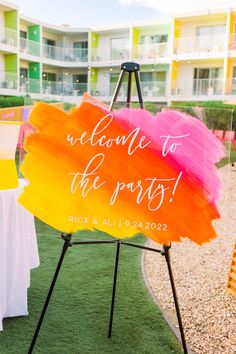 a welcome to the party sign on an easel in front of a lawn with tables and chairs