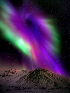 an aurora bore is seen in the night sky over snow covered hills and mountains with bright lights