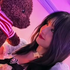 a woman with long black hair is next to a teddy bear wearing a striped shirt