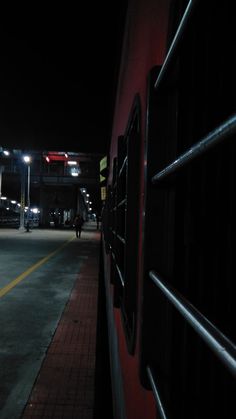 a red train parked next to a loading platform at night with people walking on it