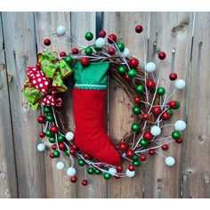 a christmas wreath with a stocking hanging from it's side on a wooden fence