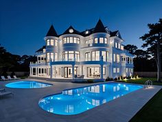 a large white house with a swimming pool in the front yard at night, surrounded by trees and lawn chairs