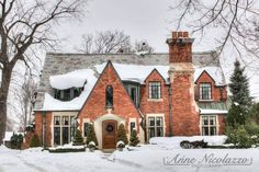 a large brick house with snow on the roof and trees around it, in winter