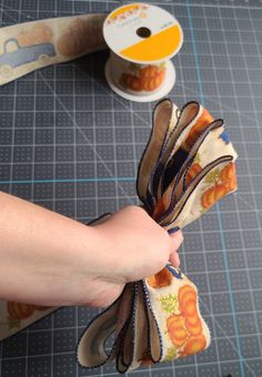 someone is holding some ribbon on top of a piece of fabric next to a spool of thread