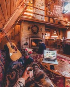 a person sitting on a couch with a laptop and coffee cup in their hand while they look at the fireplace