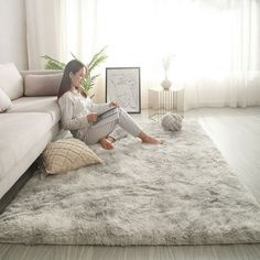 a woman sitting on top of a white rug in front of a couch with pillows