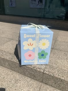 a blue gift box with flowers on it sitting on the ground next to some steps