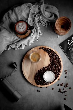 a wooden plate topped with coffee beans next to a cup of coffee and a book