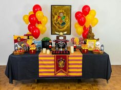 a harry potter birthday party with balloons, candy and decorations on a table in front of a hogwarts poster