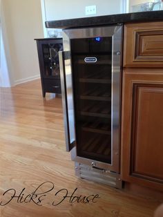 a stainless steel wine cooler in the middle of a kitchen with wood floors and cabinets