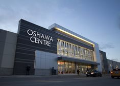 a car is parked in front of the oshawa centre building at dusk with people standing outside