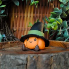 a small pumpkin wearing a hat on top of a tree stump in front of some plants