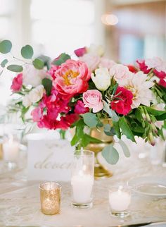 a vase filled with pink and white flowers on top of a table next to candles