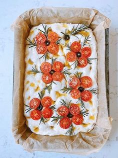 an uncooked pizza with tomatoes on it in a cardboard box, ready to be eaten