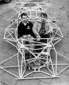 two men are sitting in a large metal structure on the sidewalk while another man stands next to them