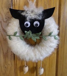 a black and white sheep head hanging from a wooden door with green leaves on it