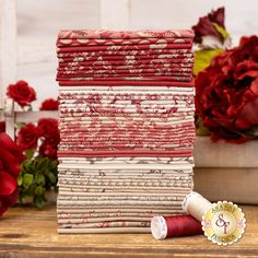 a stack of red and white fabric next to some flowers on a wooden table with a wax spool