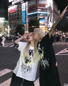 two people standing in the middle of a street with their hands up to their faces