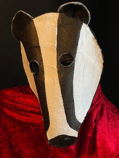 an animal mask with a red cape around it's neck and the face of a badger