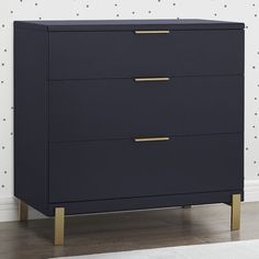 a dark blue dresser with gold handles in front of a polka dot wallpapered room