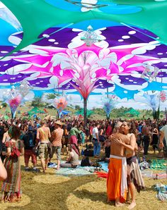 a group of people standing under colorful umbrellas at a music festival in the sun