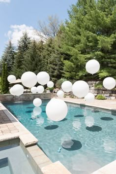 white balloons floating in the air over a swimming pool surrounded by stone steps and trees