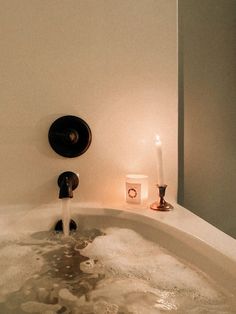 a bathtub filled with water and soap next to a lit candle on the wall