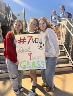 three girls holding up a sign that says kick your grass on the side of stairs