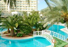 an outdoor swimming pool surrounded by palm trees and other greenery in front of a hotel