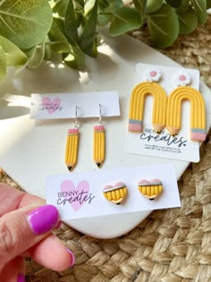 three pairs of yellow and pink earrings sitting on top of a table next to a plant