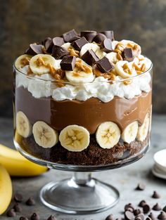 a dessert with bananas, chocolate and whipped cream on top in a glass trifle dish