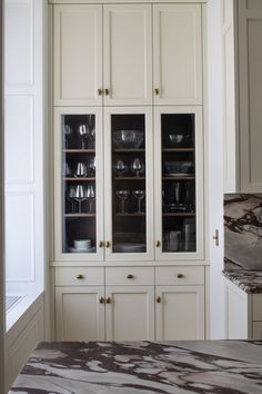 a kitchen with white cabinets and marble counter tops in front of a glass doored cabinet