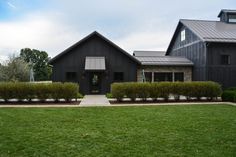 a large black house with lots of windows on the front and side of it, surrounded by lush green grass