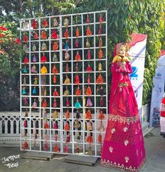 a woman in a pink sari standing next to a display of colorfully colored dolls