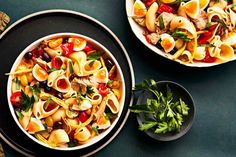 two bowls filled with pasta and vegetables on top of a green table next to a black plate