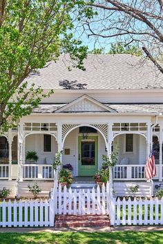 a white house with an american flag on the front porch and picket fence around it