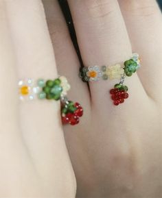 two handmade rings with beads and flowers on the fingers, one is wearing a ring that has been made to look like fruit