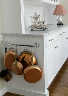 pots and pans are hanging on the wall in this kitchen with white cabinetry